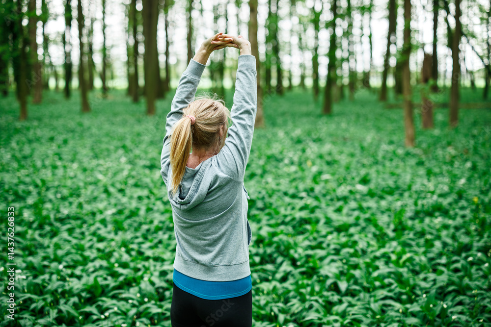 Stretching and warming up exercise. Woman lifting arms above head for back stretch in forest. Active lifestyle
