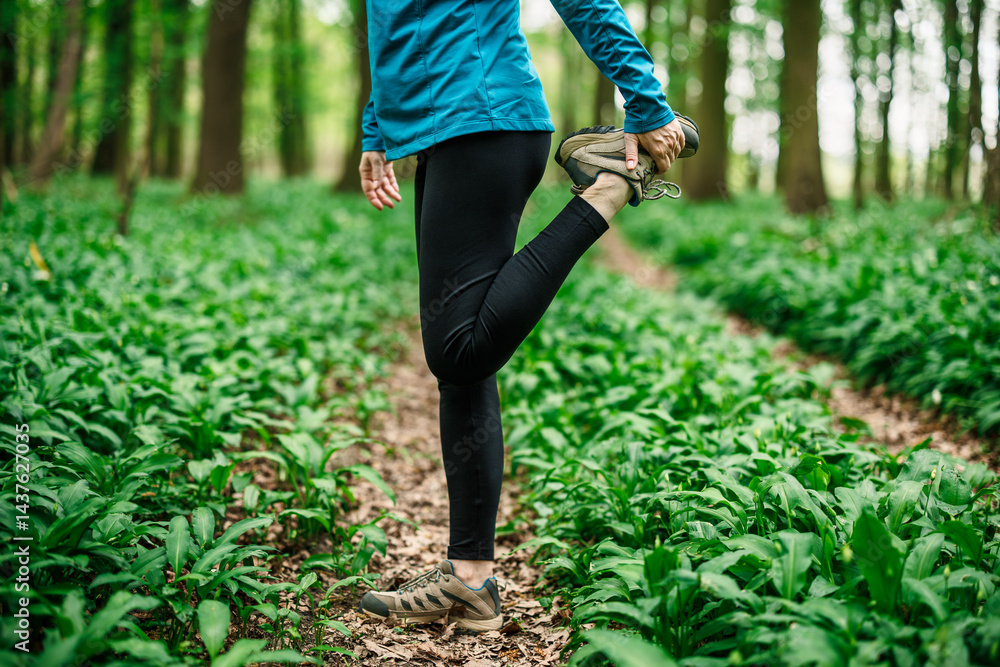 Stretching runner woman grabbing ankle in forest, sport clothing and fitness preparation outdoors. Getting ready for running
