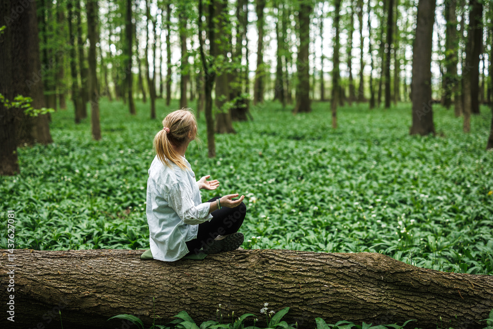 Woman doing relaxation exercise and sitting in yoga lotus position in nature. Forest bathing and meditation