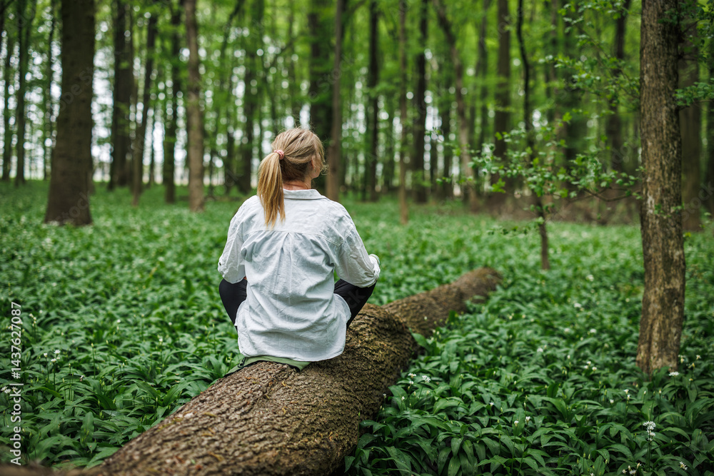 Forest therapy. Woman sitting on tree trunk in spring woodland. Mindfulness and mental wellbeing in nature