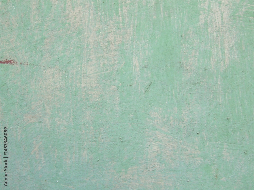 Fototapeta premium Smooth textured surface of faded mint green wall reveals layers of paint in an urban setting during daylight