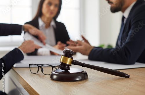 Obraz na płótnie Close up of judge's gavel and glasses on table, with lawyer meeting with group of angry, complaining clients in background, giving legal advice, and helping with problem in court. Law services concept w salonie