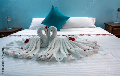 Hotel bed with towel swans, flowers, and blue pillows in a cozy room