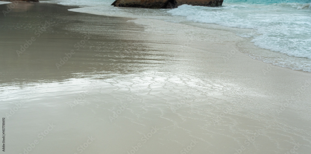 Close view of wet sandy beach with gentle ocean waves and soft reflections, captured on Praslin