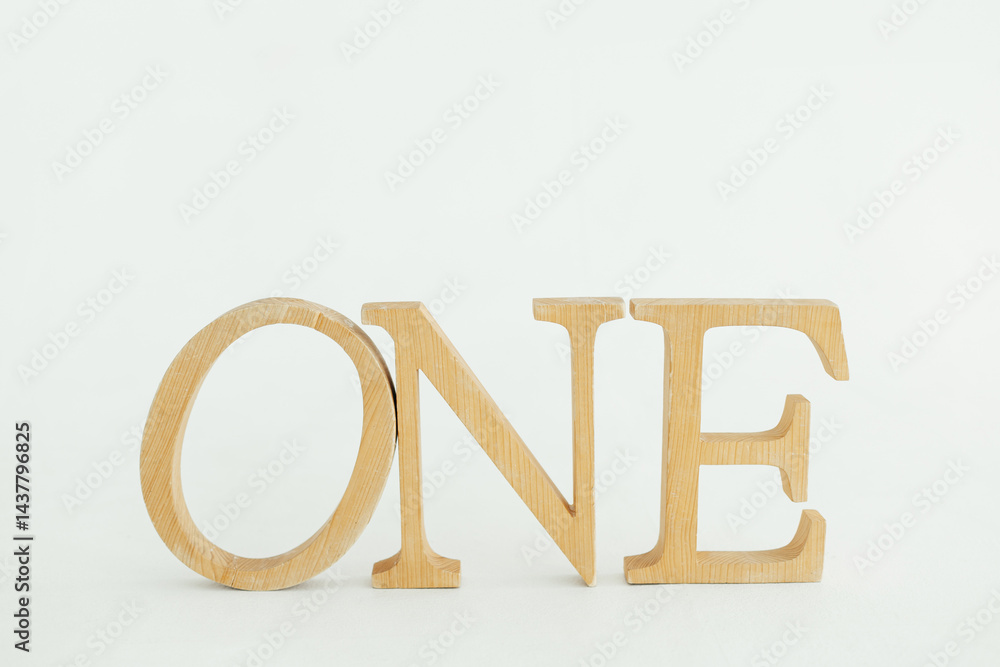 Letters carved from wood, the word one, stand on a white background
