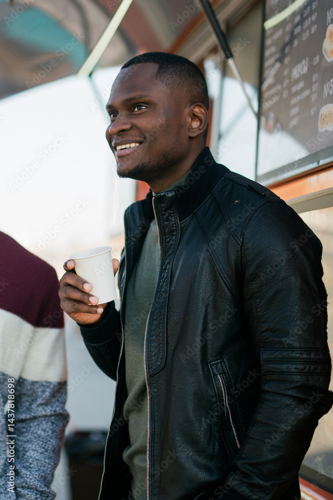 African american man smiling while drinking coffee at a food truck. Concept of urban leisure, enjoyment and positive lifestyle.