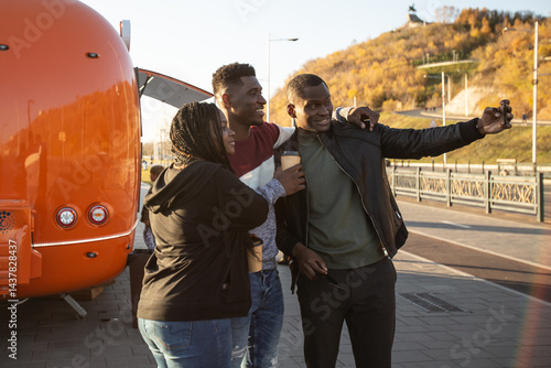 Obraz na płótnie African american friends taking selfie at sunset near food truck. Concept of friendship, technology and leisure time. w salonie