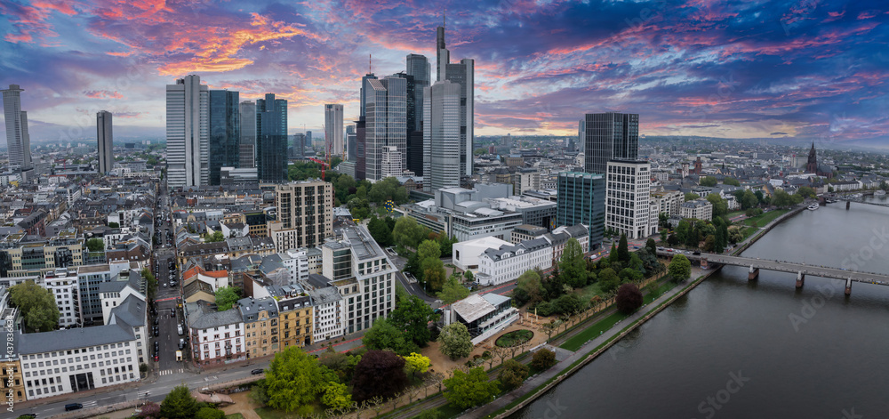 Aerial view of Frankfurt, Germany, featuring the skyline with Commerzbank Tower, the Main River, a bridge, and a vibrant sunset sky with pink and orange hues.