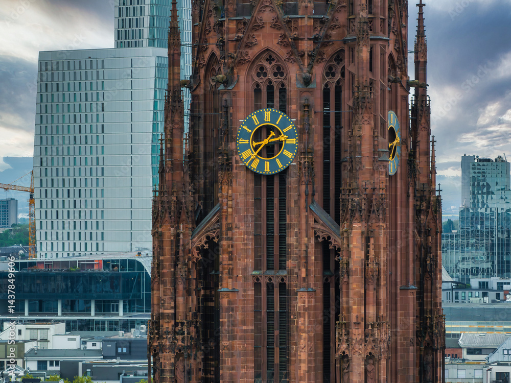 The Frankfurt Cathedral's Gothic architecture and red sandstone tower stand out against modern skyscrapers under a cloudy sky in Frankfurt, Germany.