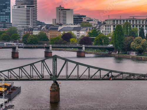 Obraz na płótnie Aerial view of Frankfurt, Germany, showcasing Eiserner Steg over the Main River, modern skyscrapers, historic buildings, and a vibrant sunset sky. w salonie