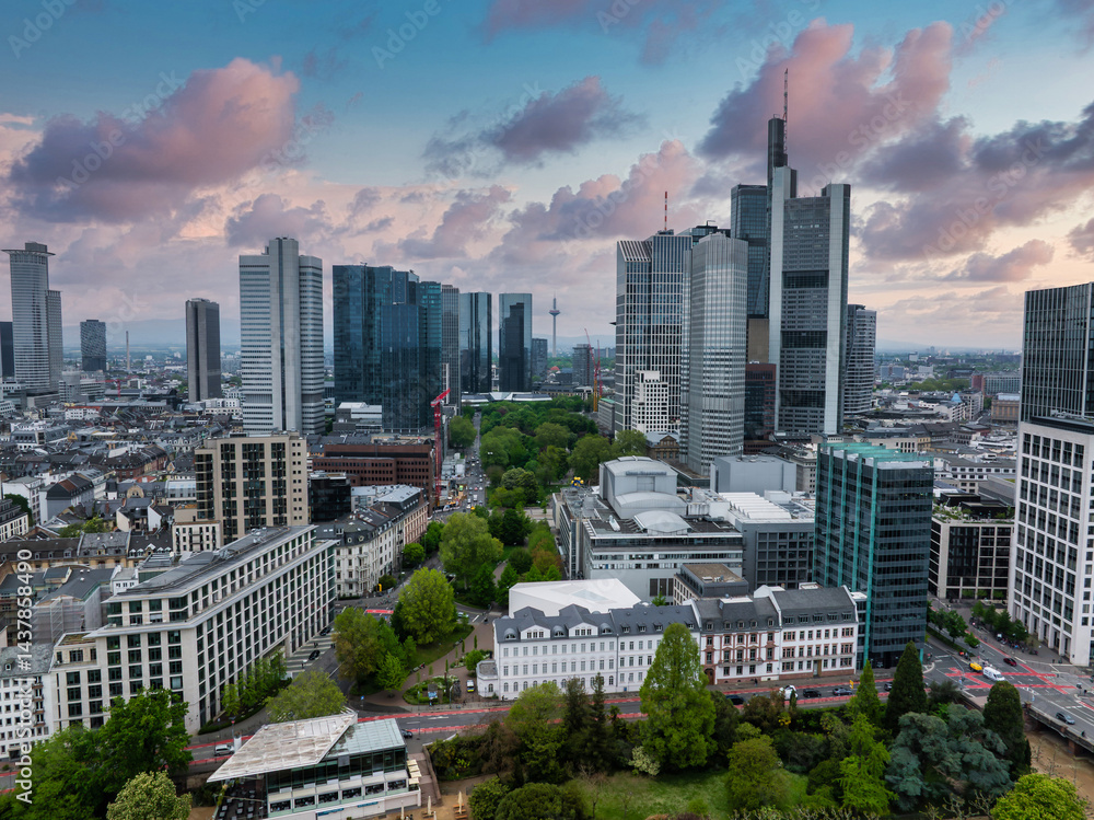 Aerial view of Frankfurt, Germany, featuring modern skyscrapers like the Commerzbank Tower, green spaces, and a sky with soft, colorful clouds.