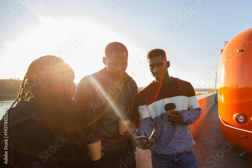 Obraz na płótnie African american friends looking smartphone while standing by river. Concept of technology, friendship, real life connection. w salonie