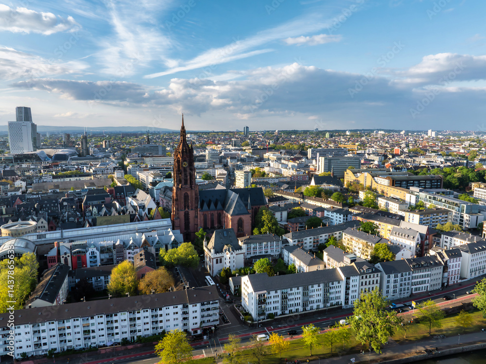 Aerial image of Frankfurt, Germany, highlighting St. Paul's Church, modern and traditional buildings, tree lined streets, and a partly cloudy sky.