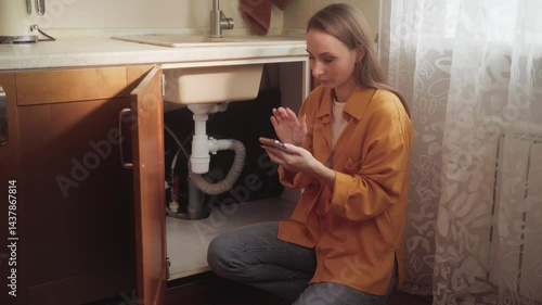 Female homeowner browsing smartphone app for selecting professional plumber, resolving kitchen sink drain clogging issue through convenient online service technology