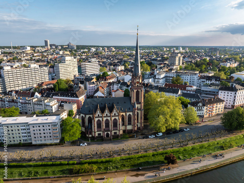 Obraz na płótnie Aerial view of Frankfurt, Germany, highlighting Dreikonigskirche's Gothic spire, the Main River, tree lined pathways, and an expansive urban skyline. w salonie