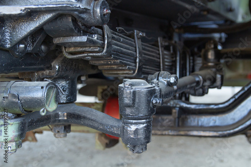 Close-up of the black suspension system of a vehicle, featuring leaf springs, shock absorbers, and various connecting rods and joints.