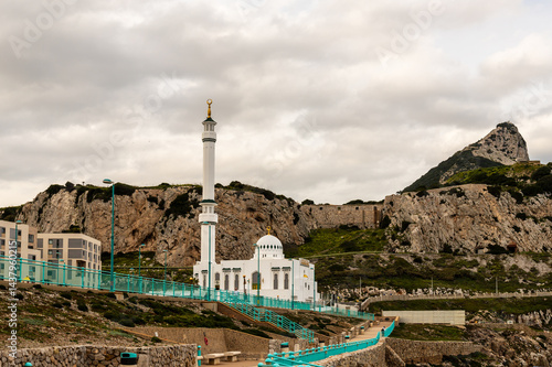 Ibrahim-al-Ibrahim Mosque with Rock of Gibraltar in Background. Scenic view of Mosque at Europa Point in Gibraltar, with dramatic cliffs and the iconic Rock of Gibraltar rising in the background.