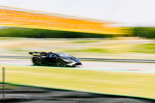 Sports car on circuit, motorsport racing, black car on race track, panning side view
