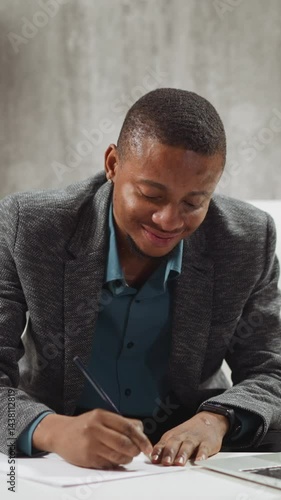 Smiling African-American guy student writes notes listening to lecture via contemporary laptop at small low table at home slow motion