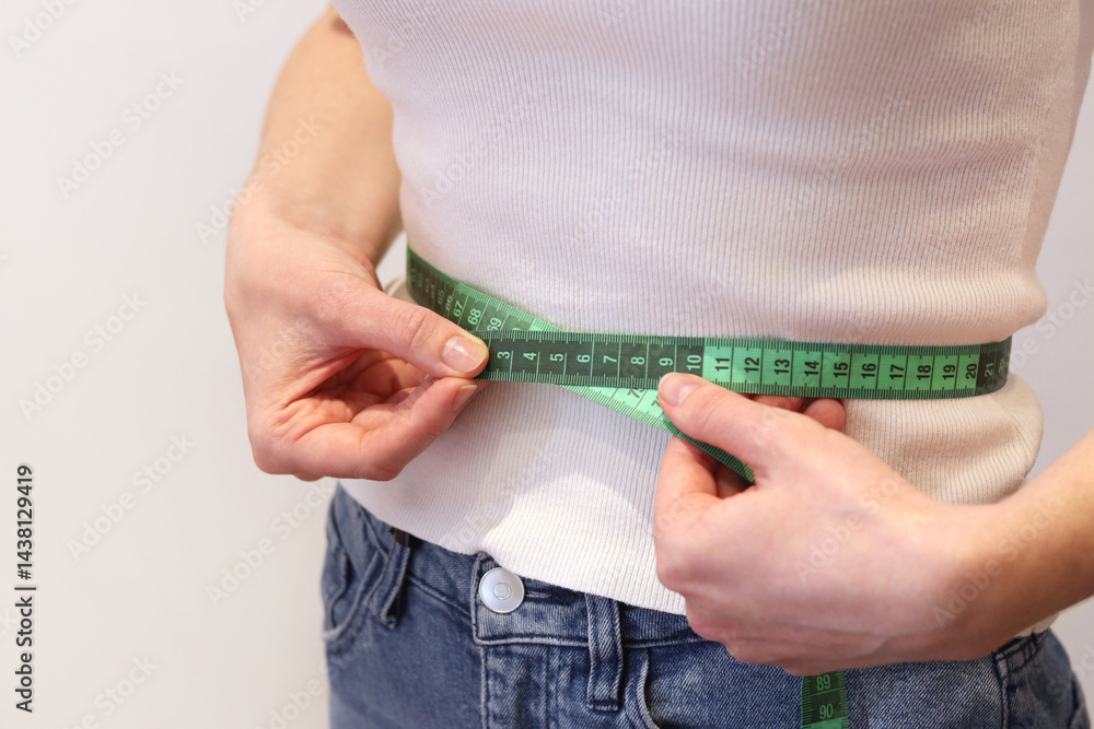 Girl measures her waist with a tape measure. Girl with a tape measure in her hands. Concept of losing weight, diet and weight control. Body volume control. Girl measures her figure after losing weight