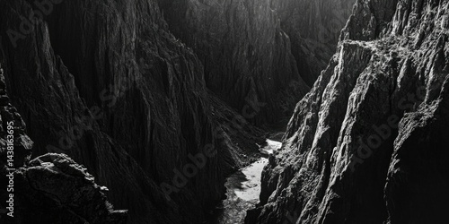 A dramatic landscape featuring a narrow, dark canyon with steep walls and a vanishing point into the distance. The image is in black and white, adding to the sense of depth and mystery. This photo