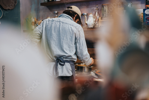 A culinary professional dressed in casual attire is cooking in a cozy kitchen setting, surrounded by utensils and cookware. The scene has a warm, inviting, and focused ambiance.