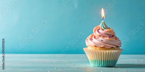 A single cupcake with pink frosting and colorful sprinkles sits on a blue wooden table, a lit candle perched atop the frosting, ready to celebrate a special occasion.