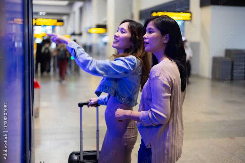 Check flight schedule on board with information display. arrival and departure board. Two Asian woman use smartphone cheking flight for travel in long weekend