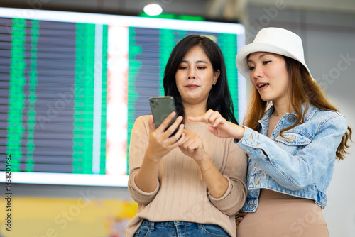 Obraz na płótnie Check flight schedule on board with information display. arrival and departure board. Two Asian woman use smartphone cheking flight for travel in long weekend w salonie