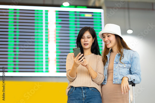 Obraz na płótnie Check flight schedule on board with information display. arrival and departure board. Two Asian woman use smartphone cheking flight for travel in long weekend w salonie