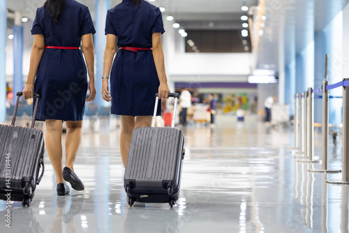 Obraz na płótnie Rear view Two woman friends walking in airport. Cabin crew, air hostess working in airplane. Service mind. Asian stewardess with suitcase at modern airport terminal. flight attendant w salonie