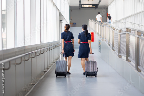 Rear view Two woman friends walking in airport. Cabin crew, air hostess working in airplane. Service mind. Asian stewardess with suitcase at modern airport terminal. flight attendant