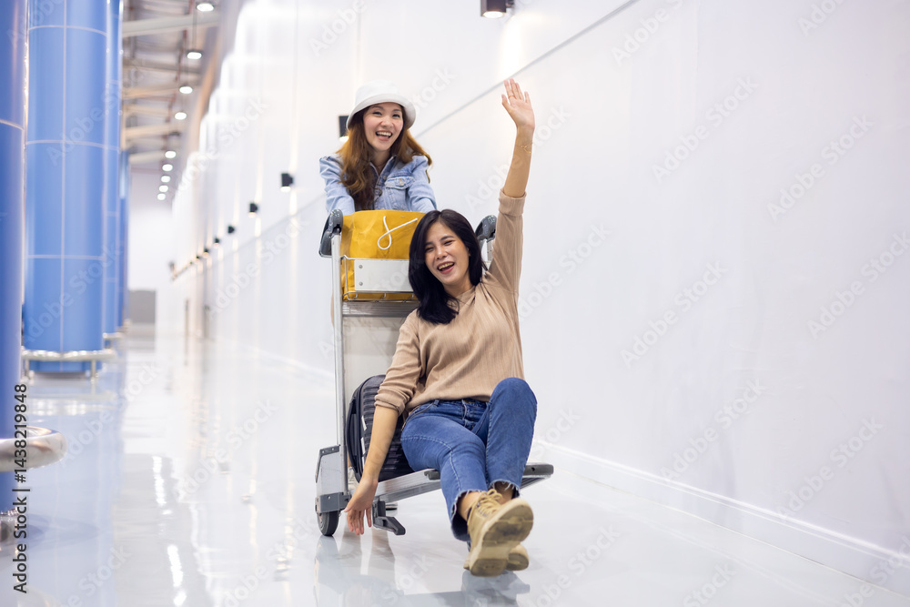 Riding baggage trolley. two Happy Asian beautiful woman passenger traveler and friends having fun with luggage at the airport
