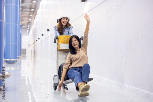 Obraz na płótnie Riding baggage trolley. two Happy Asian beautiful woman passenger traveler and friends having fun with luggage at the airport w salonie