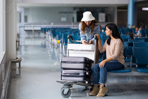 Obraz na płótnie Two Asian Woman waiting for flight at airport lounge. Happy asian woman passenger traveler waiting for departure with suitcase at modern airport terminal w salonie