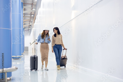 Obraz na płótnie Two Happy Asian Female Friends Travelling Together. Happy asian woman passenger traveler waiting for departure with suitcase at modern airport terminal w salonie