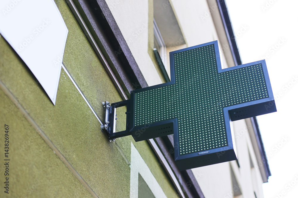 Pharmacy green cross sign. Medical symbol on building. Health care pharmacy logo. Urban architecture. Modern pharmacy signboard. Bright outdoor pharmacy advertisement. Health services concept.