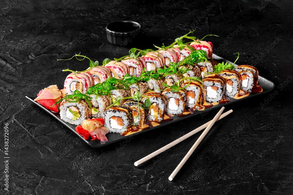 Sushi set with soy sauce, pickled ginger, wasabi, and sesame seeds on black stone background