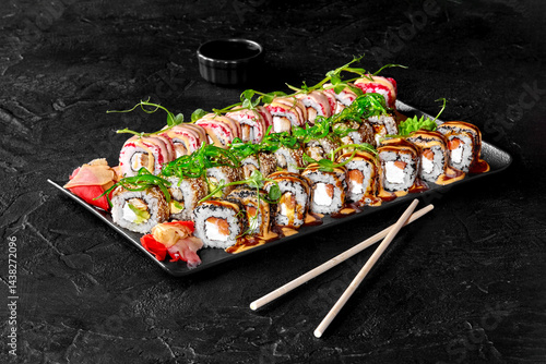 Sushi set with soy sauce, pickled ginger, wasabi, and sesame seeds on black stone background