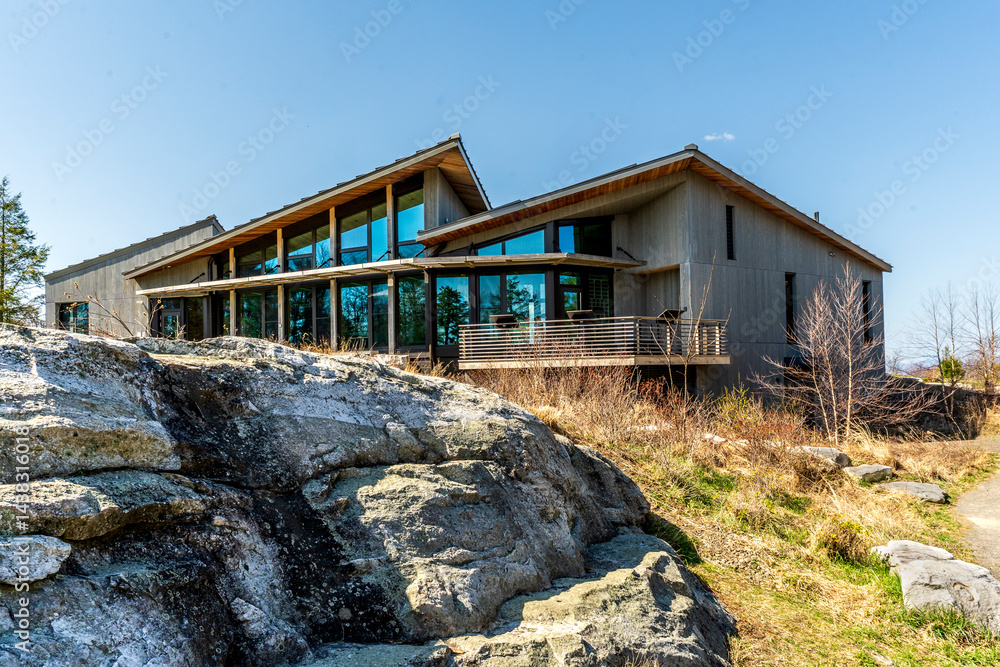 Kerhonkson, NY - US - Apr 23, 2025 Modern, wood-clad Minnewaska State Park welcome center with large glass windows sits beside stone outcrops, blending into the natural landscape under a clear sky.