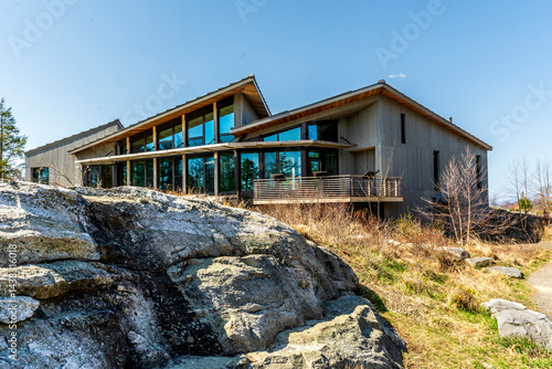 Obraz na płótnie Kerhonkson, NY - US - Apr 23, 2025 Modern, wood-clad Minnewaska State Park welcome center with large glass windows sits beside stone outcrops, blending into the natural landscape under a clear sky. w salonie