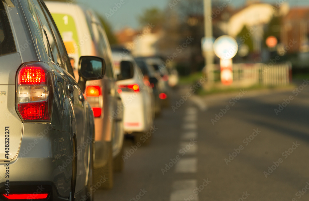 Fototapeta premium A long and linedup queue of numerous cars on a bustling city street during the beautiful golden hour of sunset
