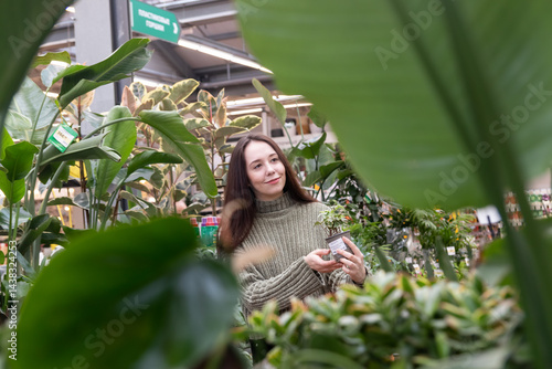In a flower shop, a girl chooses flowers for decorating a house. The buyer looks at the flowers with curiosity, getting acquainted with the assortment of the trading platform