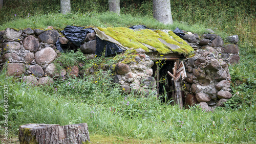 
The entrance to a stone cellar, the roof of which is partially covered with moss and black film, surrounded by green grass and trees.