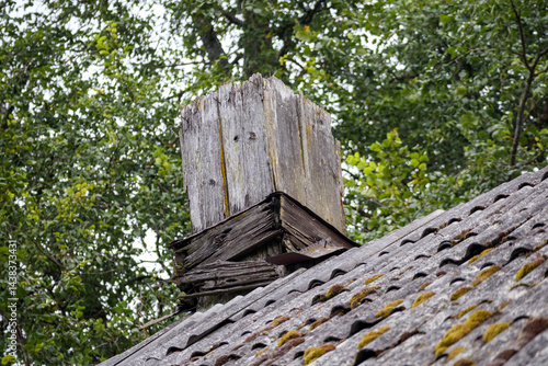 
an old, damaged chimney with peeling plaster on a slate roof surrounded by green trees.