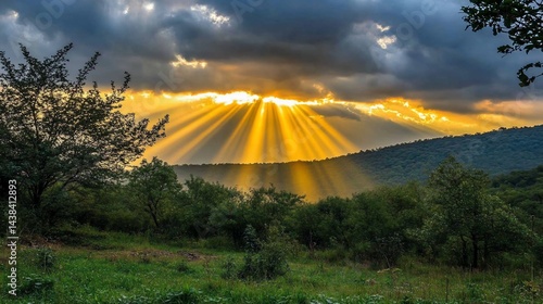 Sunbeams break through dramatic, clouded sky over a green, hilly landscape
