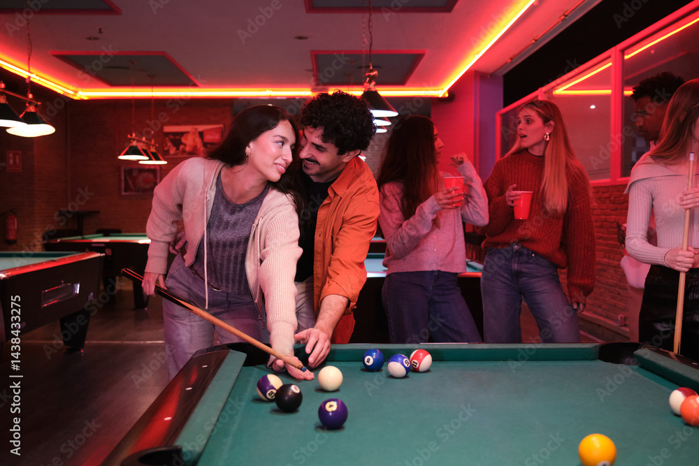 Young couple playing pool while friends cheering and drinking in nightclub