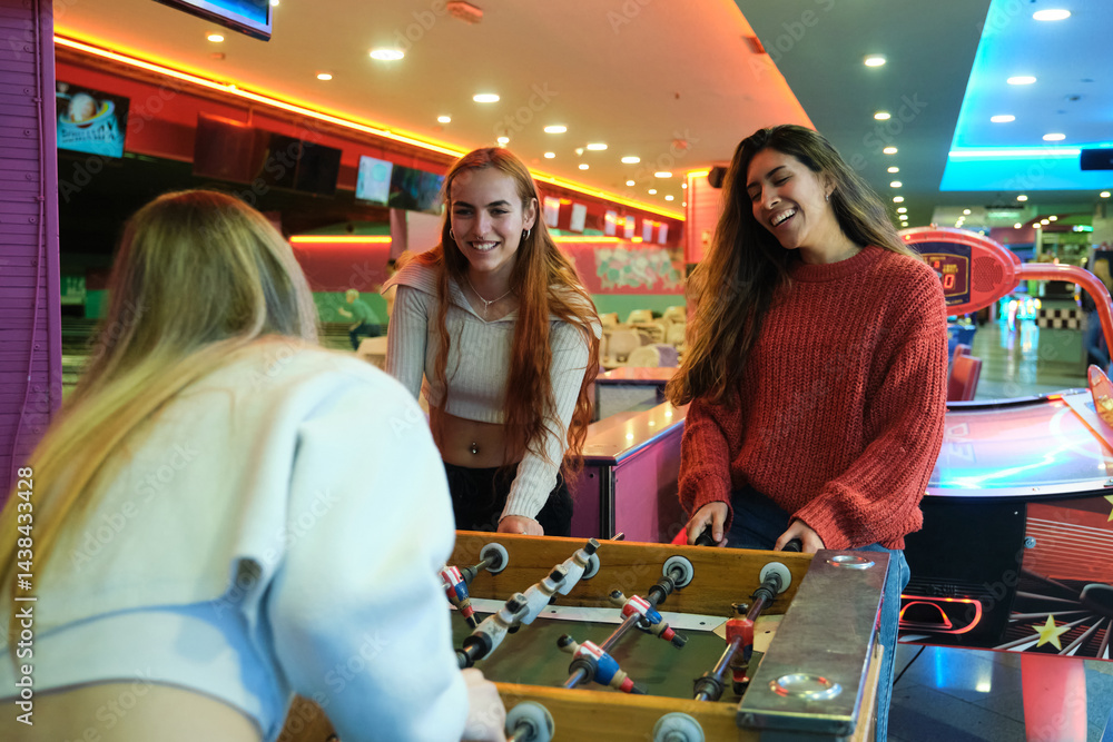 Three friends enjoying their free time playing table soccer in a colorful amusement arcade