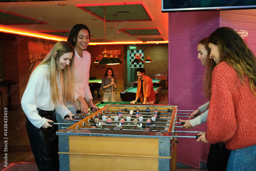 Group of friends enjoying their free time by playing table football in a colorful arcade