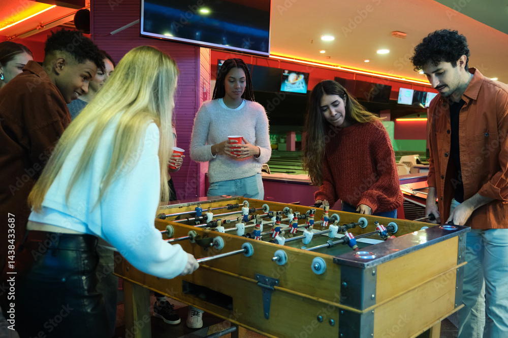 Group of friends enjoying a game of table football at a bowling alley, drinking and having fun